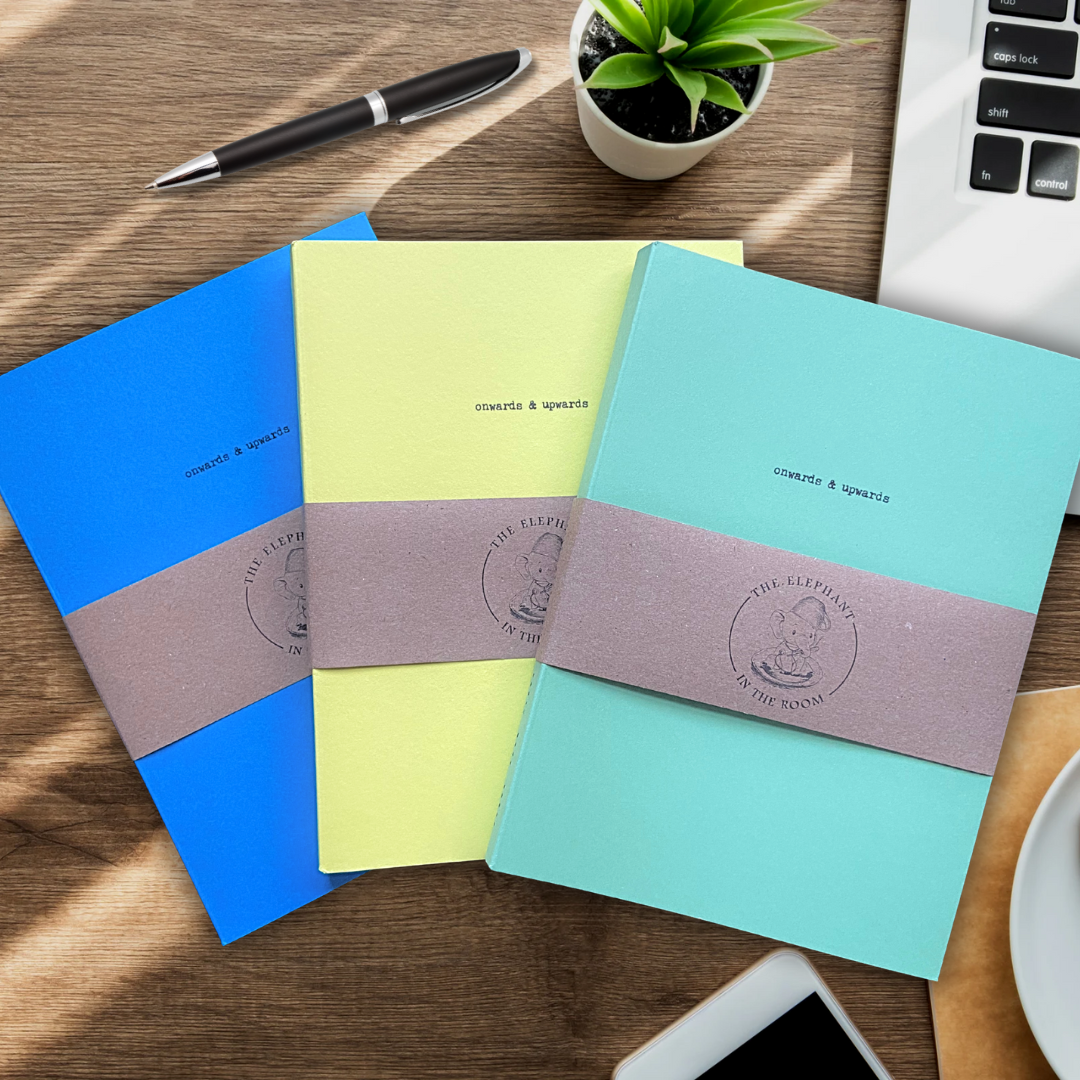 Onwards & Upwards handmade notebooks in blue, yellow and green on a desk.