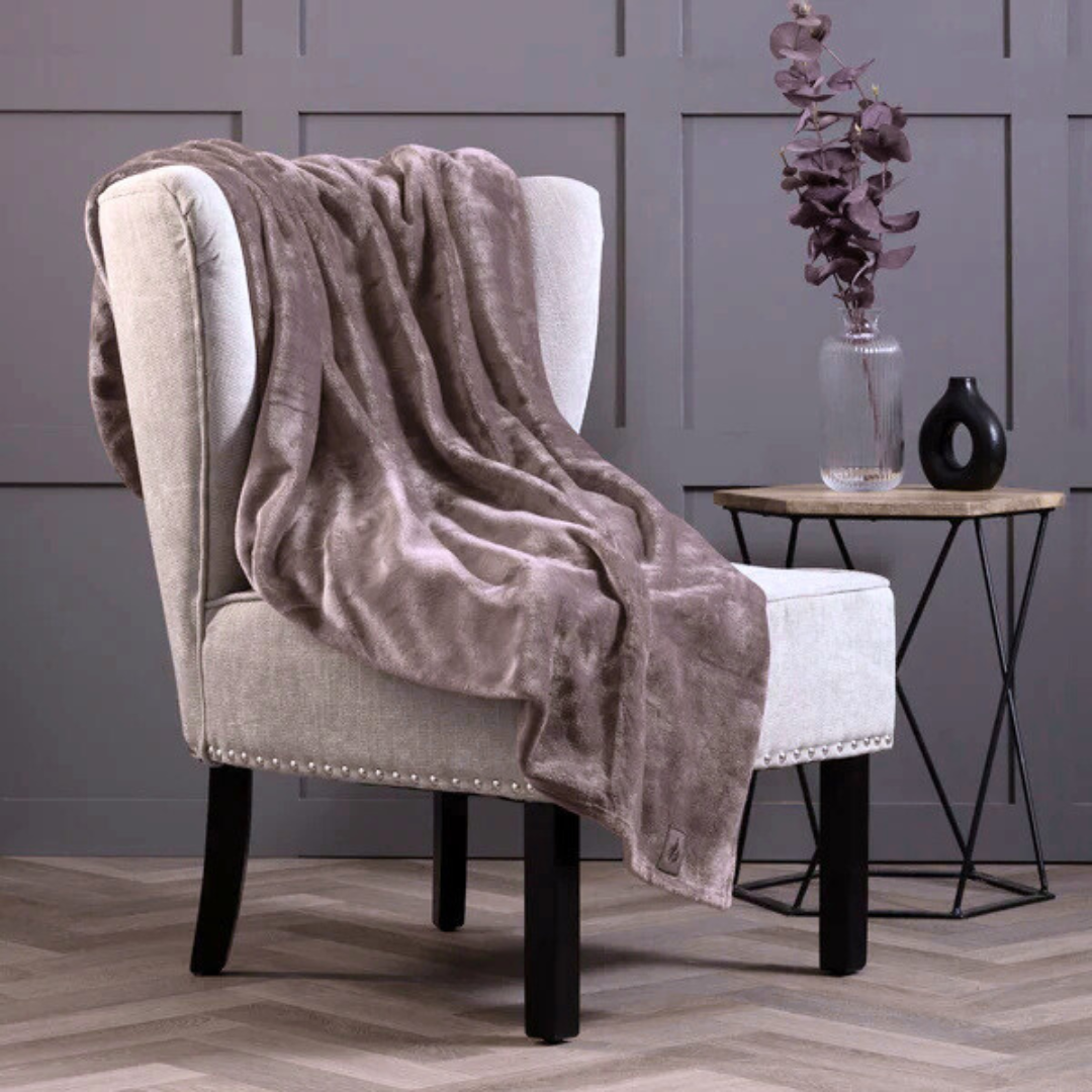 Fawn thermal blanket draped over a chair in a room with a gray wall and small table.