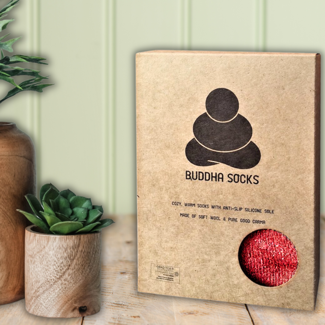 Buddha slipper Socks packaging with a red sock peeking out, placed on a wooden surface with plants.
