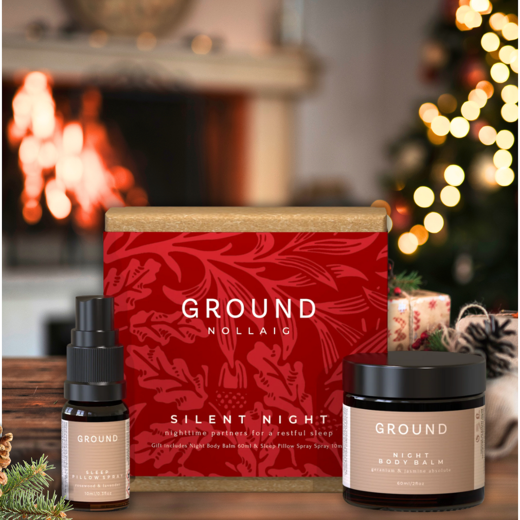Christmas gift box of natural skincare with candles and diffuser in front of a fireplace and Christmas tree.