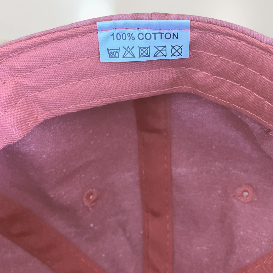 Close-up of a pink cap with a '100% Cotton' label on the back.