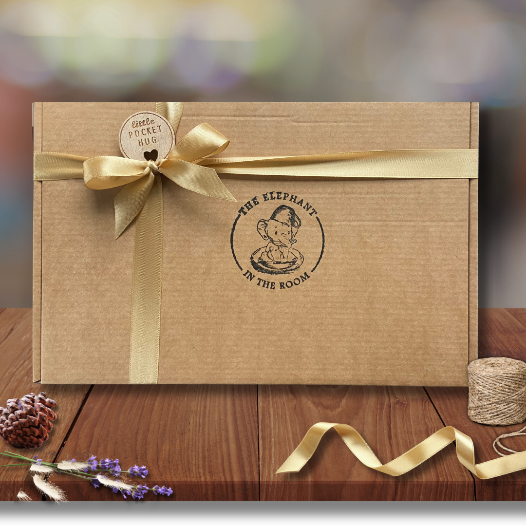 Brown gift box with gold ribbon and pocket hug charm 
featuring 'The Elephant in the Room' logo.