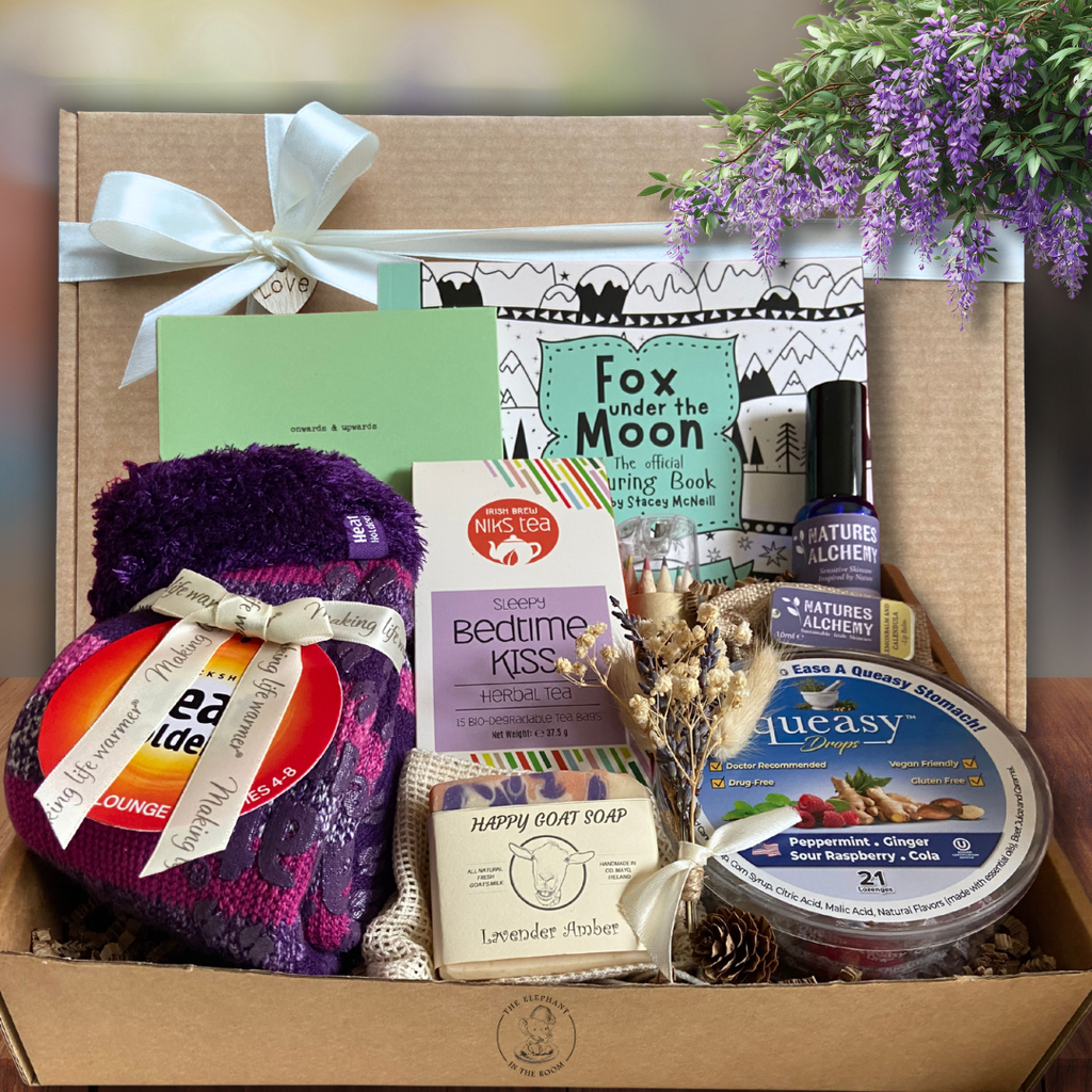 Chemotherapy hamper for her with assorted wellness gifts with a gift box and ribbon behind it.
