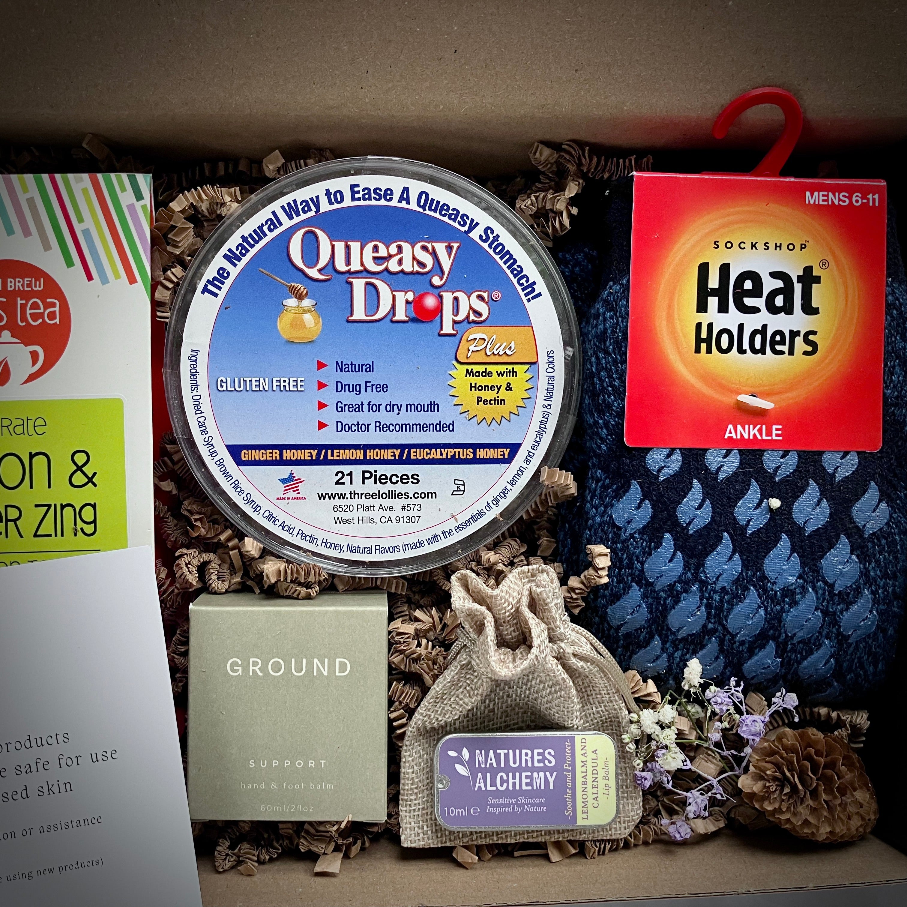 Assorted get well products including Queasy Drops, Heat Holders socks, and lip balm in a gift box 