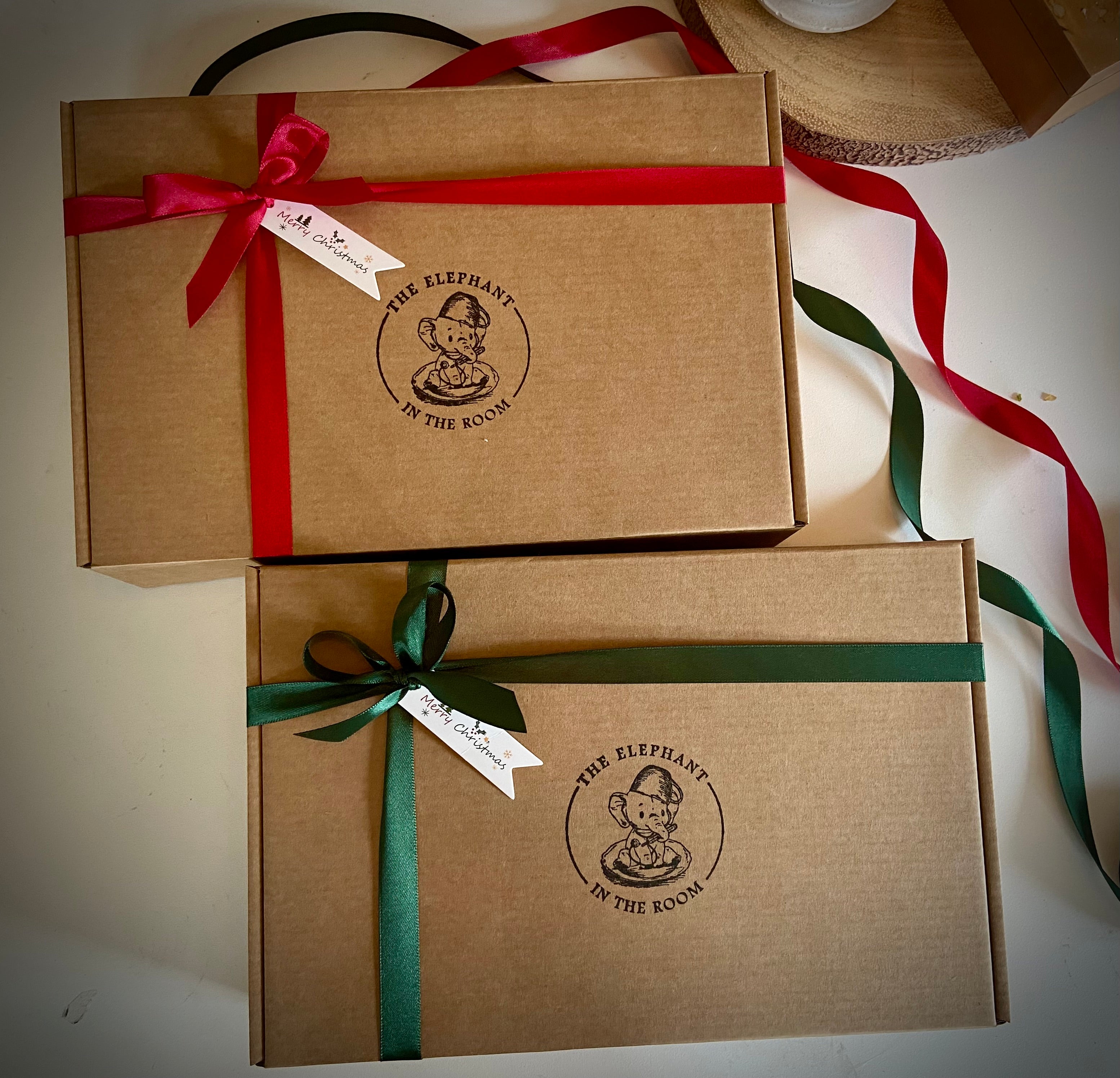 Two brown Christmas gift boxes with red and green ribbons and decorative tags on a white surface.