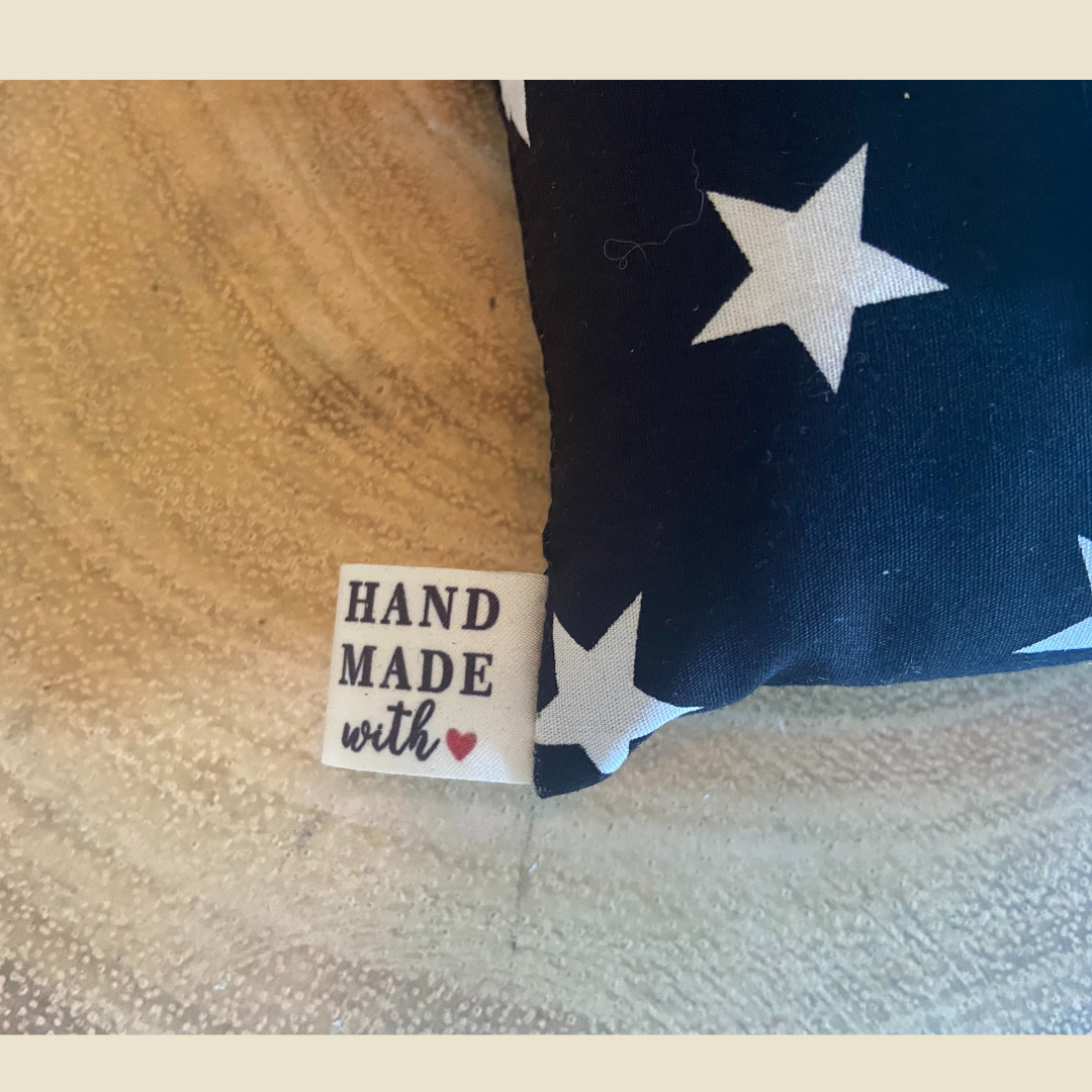 Close-up of a 'Hand Made with Love' tag on a car seat-belt cushion in black fabric  with white stars.